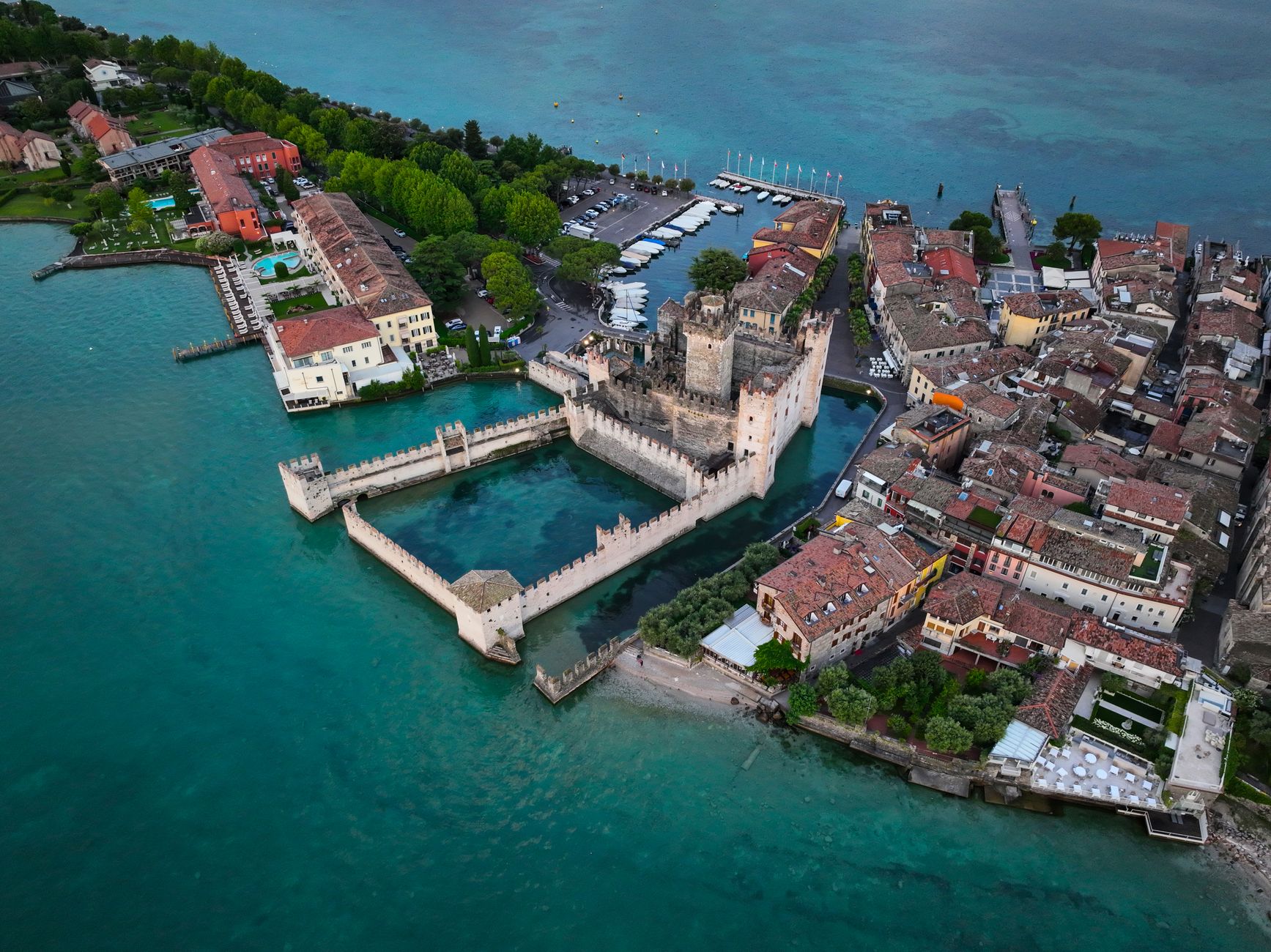 Aerial view of Scaliger Castle in Sirmione with vibrant turquoise waters, showcasing Italian architecture and historical charm.