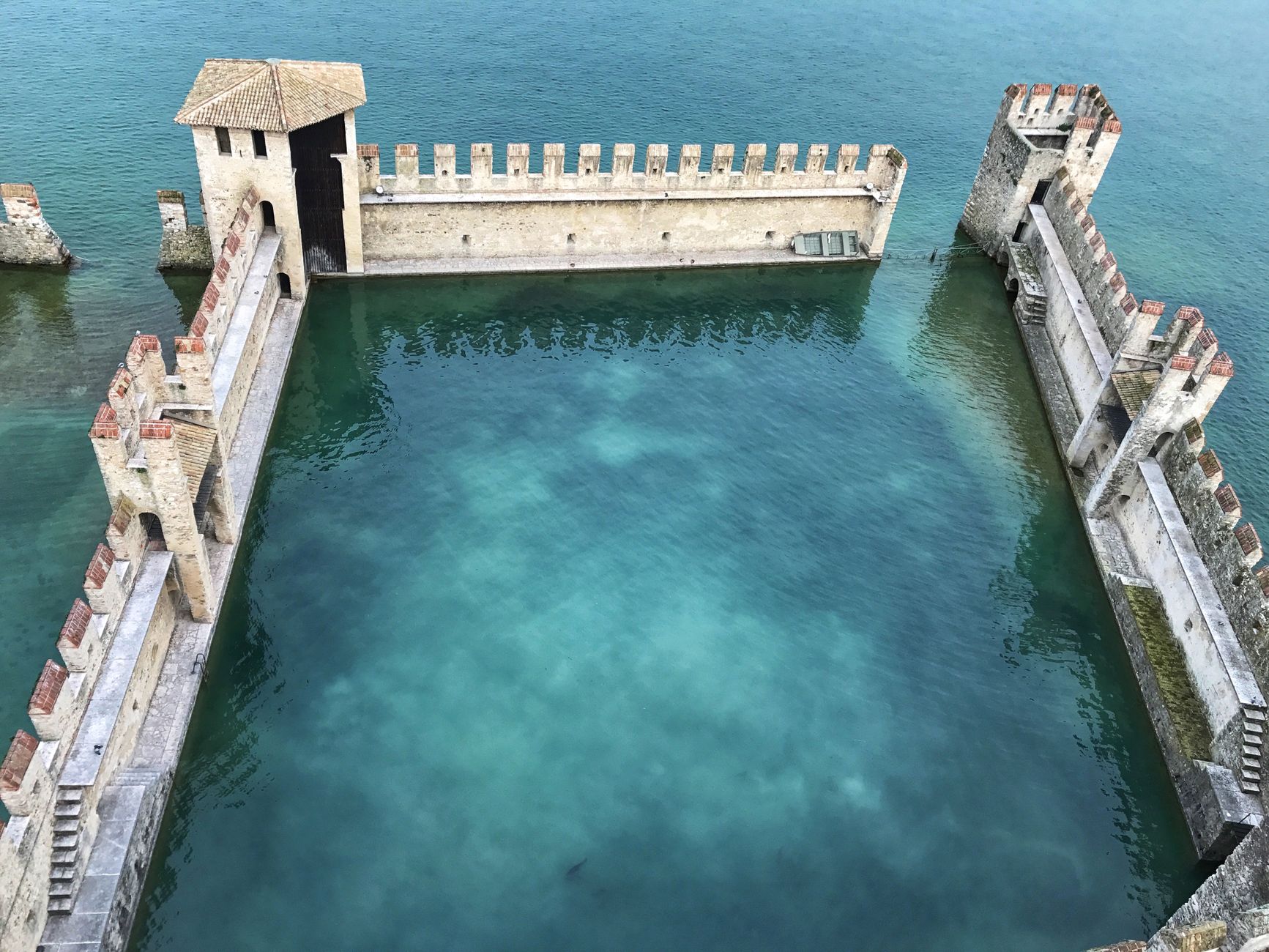 Aerial view of Scaliger Castle's fortified walls and clear turquoise waters in Sirmione, Italy.