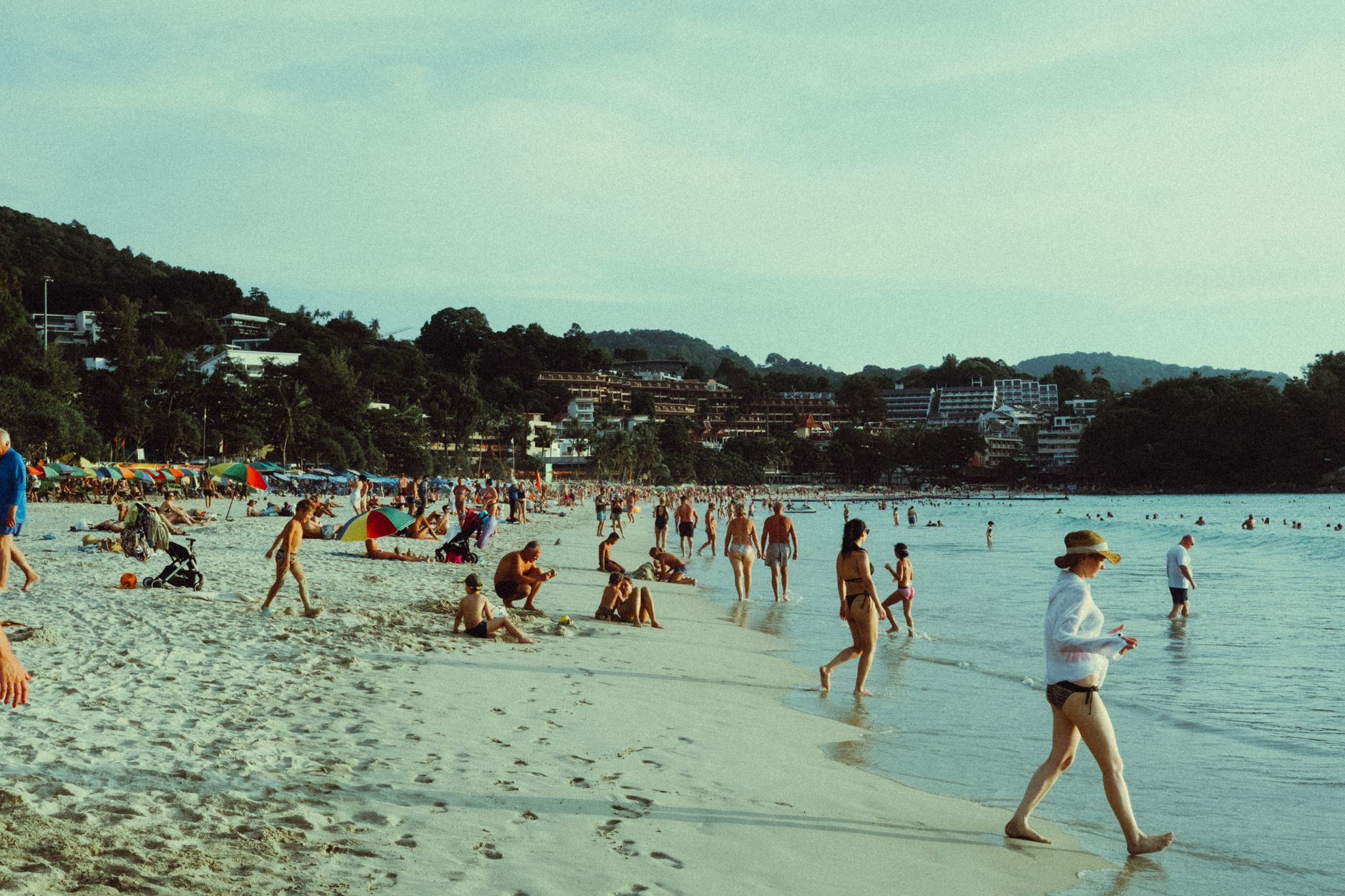 People enjoying a vibrant day at a tropical beach, with umbrellas and lush greenery.