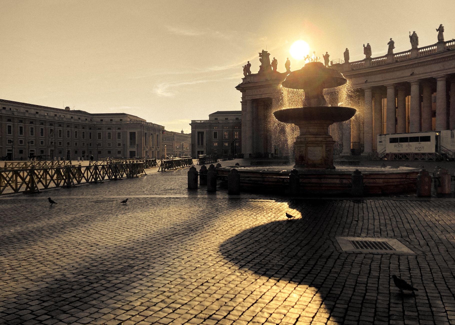 Beautiful sunrise over St. Peter's Square fountain in Vatican City, highlighting historic architecture.