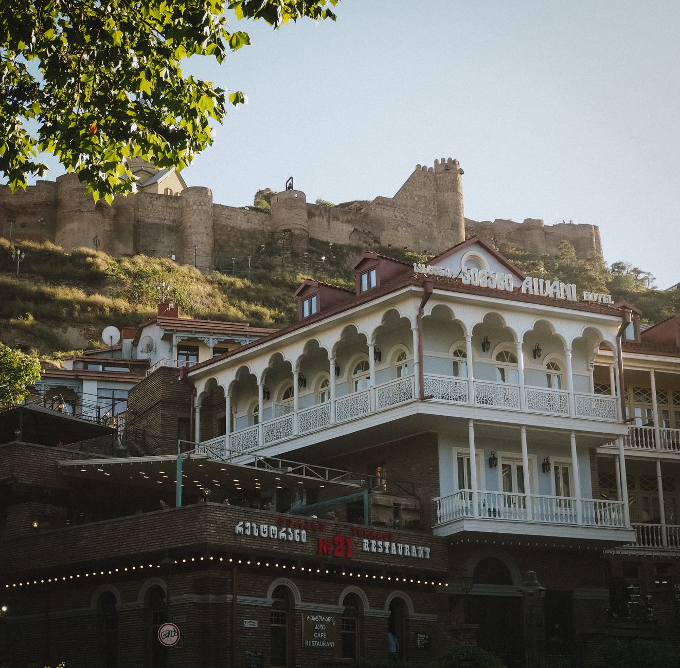 View of Narikala Fortress atop a hill with a traditional hotel in Tbilisi, Georgia.