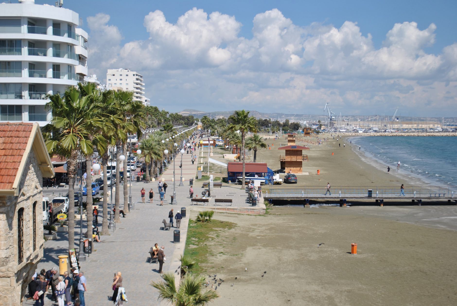 Scenic view of Larnaca promenade and beachfront with people walking and palm trees.